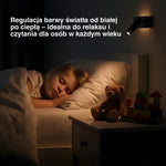 Dziecko śpiące na łóżku obok stolika z zabawkami, nad nim czarna lampa ścienna.