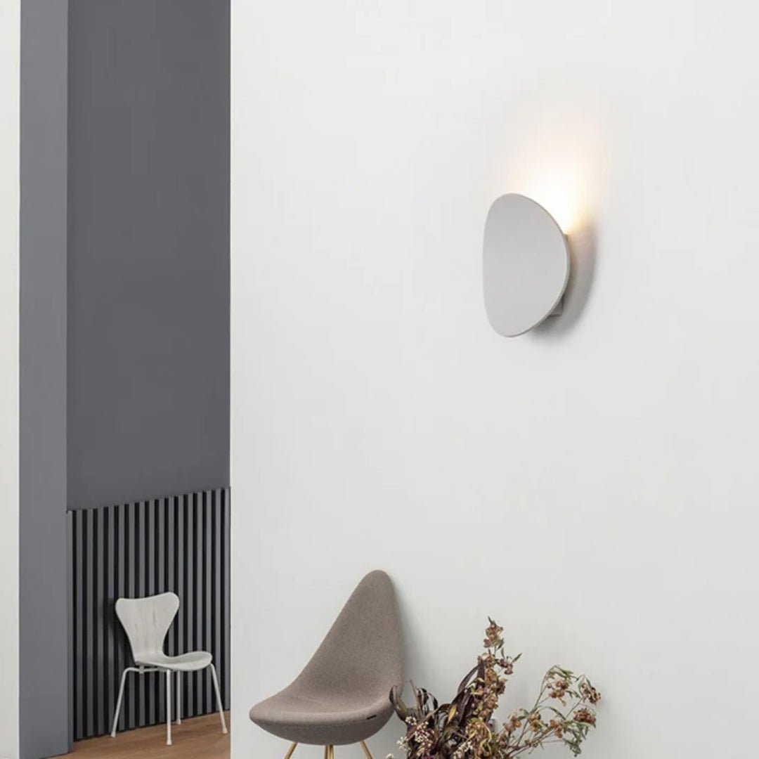 Biała metalowa lampa łazienkowa nad dwoma krzesłami i rośliną